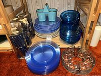 Photo showing blue plastic plates, cream plastic plates, blue glass bowls, silverware in glass holder, and turquoise metal bucket caddy.