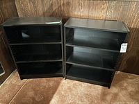 Two black lower bookshelves side by side, showing front view with three shelves each.