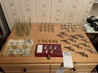 Large assortment of various metal dining table place card holders arranged on a wooden surface, showing multiple designs including Eiffel Towers, dolphins, pineapples, and additional round holders.