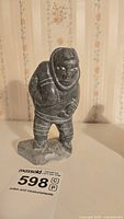 Front angle of soapstone figure showing man wearing hooded clothes and carrying a seal on his back, minor scratches visible.