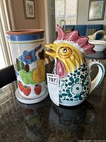 Side-by-side photo of the ceramic rooster pitcher and the floral/fruit ceramic wine cooler with coaster on a table.