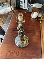 Full view of the bronze metal lamp base with the socket and harp, on a wooden table with some candles and other items in background.