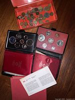 Three black coin cases with Canadian collector coin sets and orange container with loose coins on wood floor