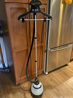 Full view of the Conair clothes steamer standing upright on a hardwood floor showing the hanger, telescopic pole, steam hose, and base.
