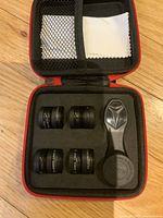 Open protective case showing four photography lenses, lens cleaning blower, and cleaning cloth inside slots and mesh pocket