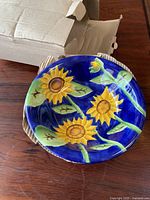 Top view of one bowl showing bright hand painted sunflowers with green leaves on a blue background and cardboard packaging