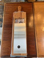 Full view of the Gigi Cool charcuterie board sealed in plastic, showing the wooden board with handle and the stainless steel surface.