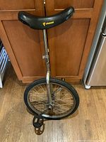 Full view of unicycle upright on wooden floor, showing chrome frame and black Viscount saddle.