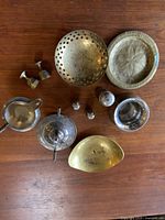 Top down view of all items arranged on wood surface: brass and copper pots, perforated brass dish, hammered brass tray, silver plate cream, sugar, salt and pepper shakers, and candle holders.