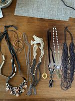 Top-down photo showing 10 vintage costume jewelry necklaces and bracelets arranged on a wooden surface