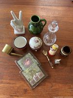 View showing all eleven vintage decorative items on wood surface including glass coasters, ceramic pieces, small brass scoop, spoon, and glass decanter