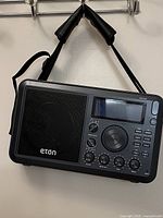 Front view of black Eton Elite Field radio hanging on hook, showing speaker, control knobs, and display screen.