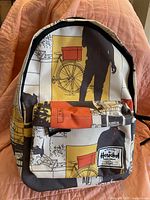 Front view of the backpack showing the colorful print with silhouetted figures, bicycle, and urban scenes.