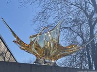 Front view of the large amber yellow freeform glass sculpture on outdoor surface with sky background, showing shape and clarity.