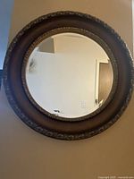 Front view of the round mirror showing black frame with gold decorative edges and reflective glass surface.
