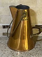 Copper jug with brass handles, front angled view on tiled countertop.