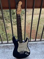 Full front view of blue Squier Bullet Stratocaster guitar leaning against railing outdoors