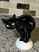 Front view of vintage black Goebel Hummel cat figurine with missing tail on white base showing green eyes and alert pose.