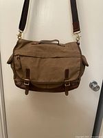 Front view showing brown canvas fabric, dark brown leather trim, two buckle straps at the front, and shoulder strap attachment.