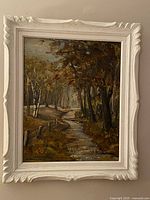 Frontal view of vintage original oil painting showing autumn landscape with trees, stream, and fence in a carved painted wooden frame.
