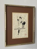 Framed vintage original art print by Enook Manomie showing Indigenous young person hunting a seal, detailed close-up of artwork title and signature.