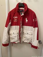 Front view of red and white jacket showing full-zip closure, snap storm flap, front pockets and CAN/Cup embroidery