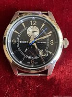 Front view of the Timex watch showing black dial, power reserve indicator, date window, and hands.