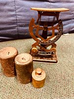 Metal antique bi-lateral scale with three accompanying cylindrical weights on carpeted surface.