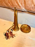 Overall view of the World War I military bugle and the trench art paperweight side by side on a wooden surface.