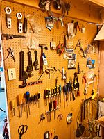 Pegboard wall showing assorted hand tools hung and organized including pliers, wrenches, screwdrivers, utility knives and clamps