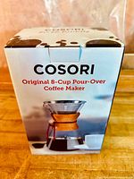 Box front showing branding and image of the pour-over coffee maker with glass carafe, wooden collar, and metal mesh filter.