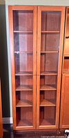 Front view of tall IKEA Billy bookcase with two glass doors and multiple shelves showing cherry wood finish.