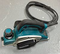 Side view of Makita electric planer showing adjustment knob, front and rear handles, and power cord coiled at rear.