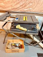Front view of table saw mounted on fold & roll stand with wooden box of saw blades.