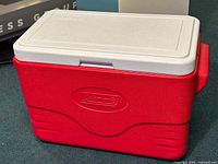 Full view of the red Coleman cooler showing the white lid and molded logo on the front.