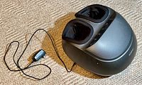 Angled side view showing foot massager with power adapter on carpeted floor.