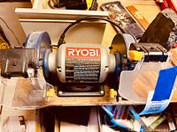 Front angle showing Ryobi BG612 label and one grinding wheel with attached safety shield and tool rest.