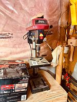 Full view of drill press mounted on wooden base with original box beside it