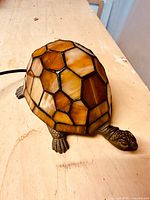 Side and front view of turtle-shaped lamp with stained glass shell in amber tones and metal legs and head.