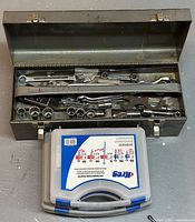 Open metal tool box showing various hand tools arranged inside along with a closed plastic box of screws in front
