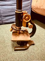 Side angle showing brass focus knobs, black cast metal arm, and base of microscope along with stage.