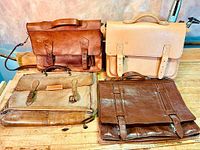 Four vintage leather briefcases in various shades of brown and tan, displayed on a wood surface.