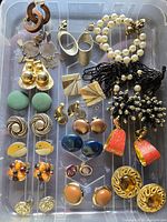 Top-down view of assortment of 20 pairs of clip-on earrings showing a variety of styles including gold-tone, faux pearl, fabric, and resin earrings.