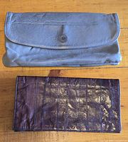Two vintage leather wallets laid flat on wooden surface. Top wallet is grey with flap and snap button. Bottom wallet is dark brown, soft leather.