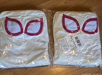 Two white superhero costumes, folded and sealed in packaging with pink mesh eye shapes and red/pink outlines visible