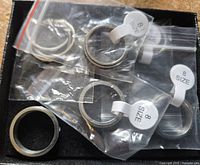 Six individual metal fidget rings in plastic bags, all size 8, arranged in a black box.
