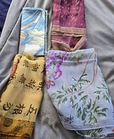 Four silk scarves arranged on a surface showing various color schemes and designs including florals and script.
