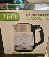 Photo of boxed TRU 1.7 liter glass kettle with boiling water image on box front showing product features such as heat resistant glass and automatic shut off.