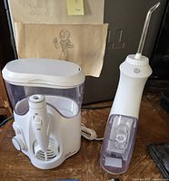 Waterpik WP-150 Series water flosser with base, power cord, and one attached sprayer head shown on wooden surface