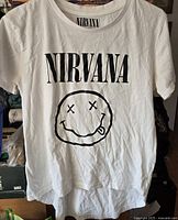 Full frontal image of the white Nirvana t-shirt showing the brand name and smiley face print.